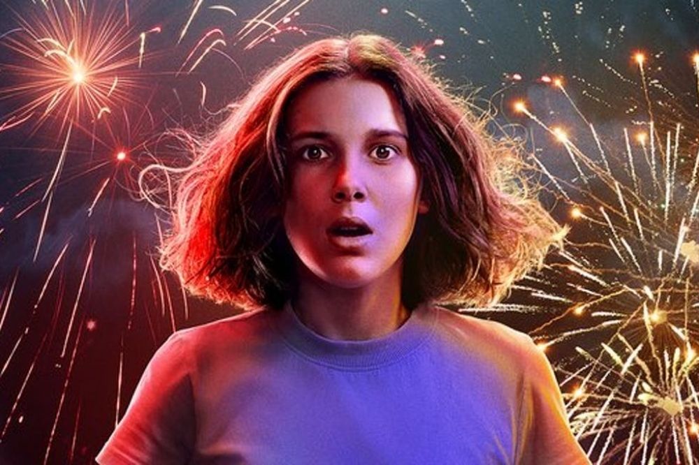 Foto de divulgação da série Stranger Things. Nela, aparece a personagem Eleven com blusa cinza e um cenários de fogos de artifícios ao fundo.