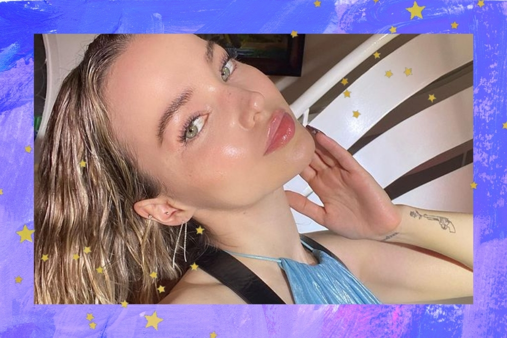 Foto da Dove Cameron com as bordas azuis e detalhes de estrelinhas dourada. Na foto ela usa um vestido azul, cabelo solto e maquiagem com efeito natural. Ela está com a mão esquerda no rosto, olha para a câmera e não sorri.