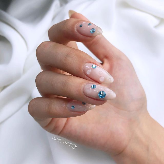 Foto de uma mão com as unhas longas e detalhe de brilho azul e gotinhas de água de gel 3D.