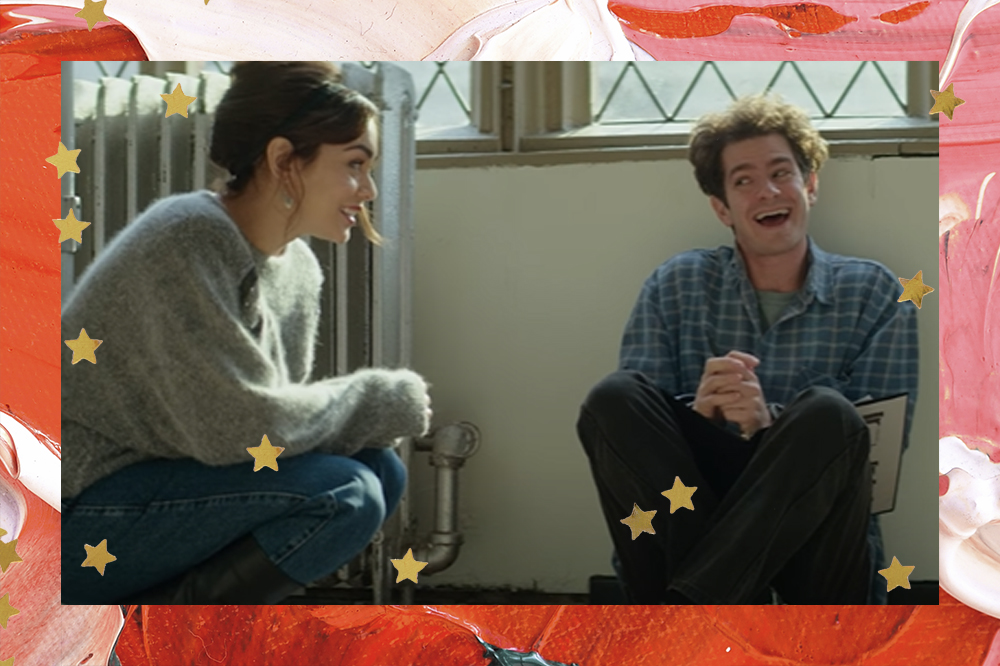 Vanessa Hudgens e Andrew Garfield em cena de Tick, Tick... BOOM!, o novo musical da Netflix; Vanessa está agachada ao lado de Andrew, que está sentado com as costas encostadas na parede com uma janela acima de sua cabeça; os dois estão se olhando e sorrindo enquanto conversam; a margem é uma textura de tintas em tons de vermelho, rosa e branco com estrelas amarelas como decoração