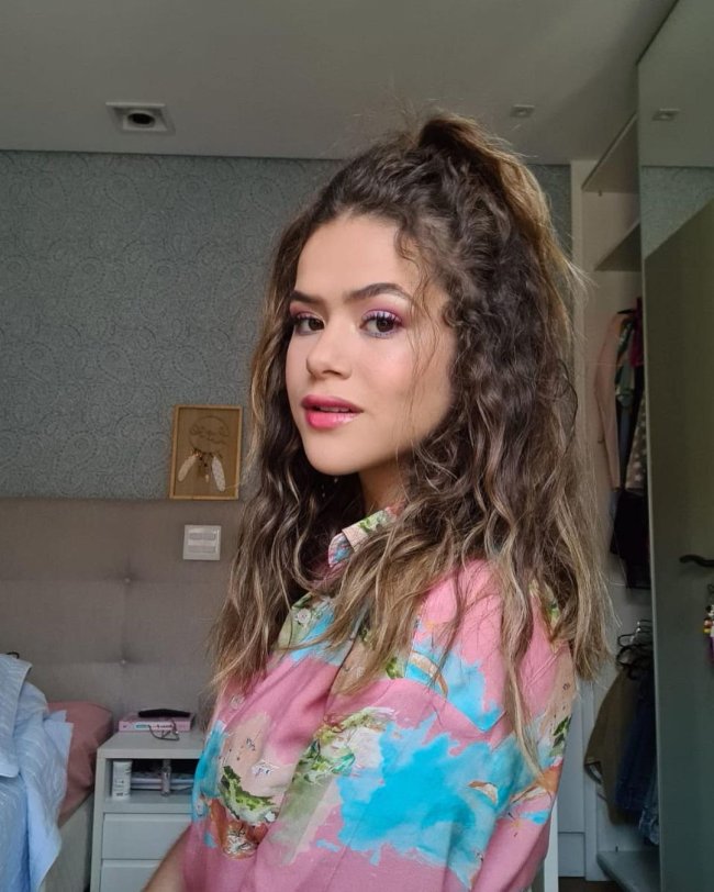 Penteado meio preso com Maisa Maisa posando para foto olhando de lado com blusa com degrade azul e rosa e expressão levemente sorridente.