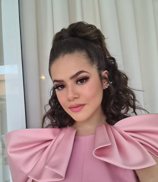 Maisa posando com penteado meio preso Maisa posando para selfie com expressão sorridente e usando blusa com manga bufante rosa.