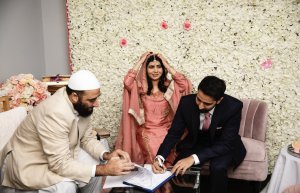 Foto do casamento de Malala. A família está reunida em frente a uma parede de rosas brancas. Todos sorriem.