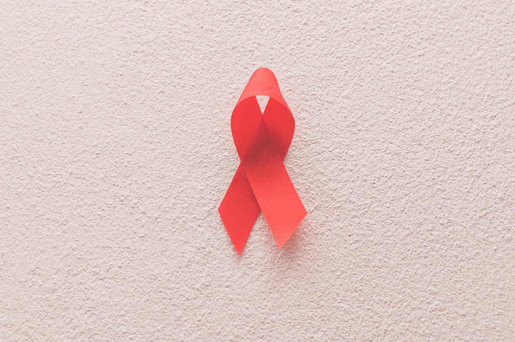 Foto de uma parede rosa e, presa a ela, uma fita vermelha, símbolo do combate a Aids