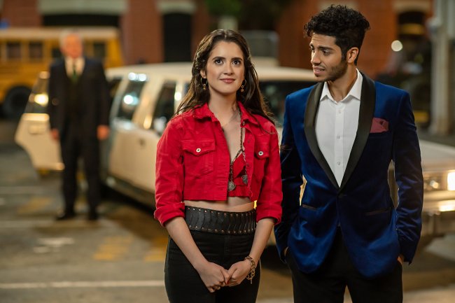 Laura Marano como Izzy e Mena Massoud como princípe Thomas em Tratamento de Realeza, da Netflix; os dois estão andando na rua; Laura olha para frente sorrindo levemente enquanto Mena olha para ela com admiração