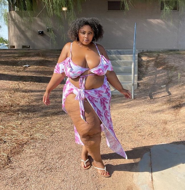 biquini-com-saia Foto de uma mulher. Ela usa um biquíni branco com estampa rosa e canga com a mesma estampa amarrada na cintura. Ela olha para a câmera e não sorri.