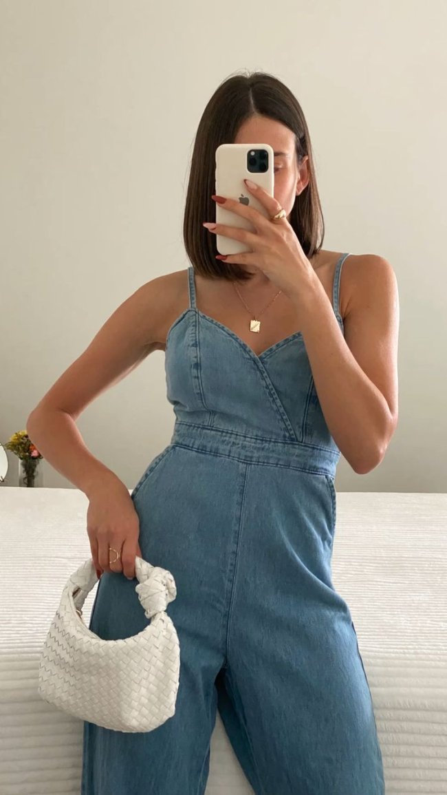 macacao-jeans-levinho Selfie de uma mulher na frente do espelho. Ela usa um macacão jeans e bolsa branca.