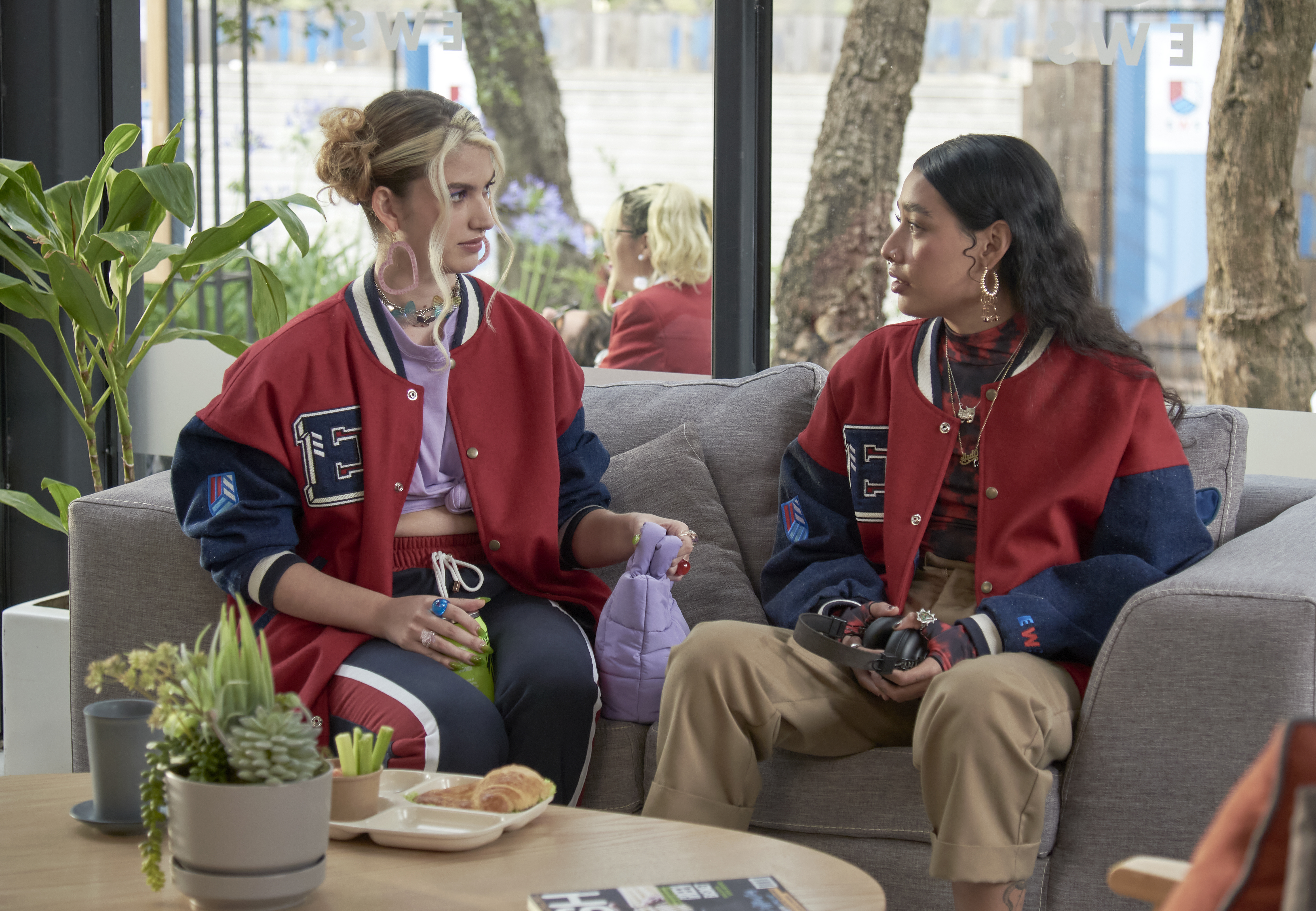 cena-rebelde-netflix-uniforme-05 As personagens Emilia e Andi sentadas em sofá em cena da série Rebelde, da Netflix