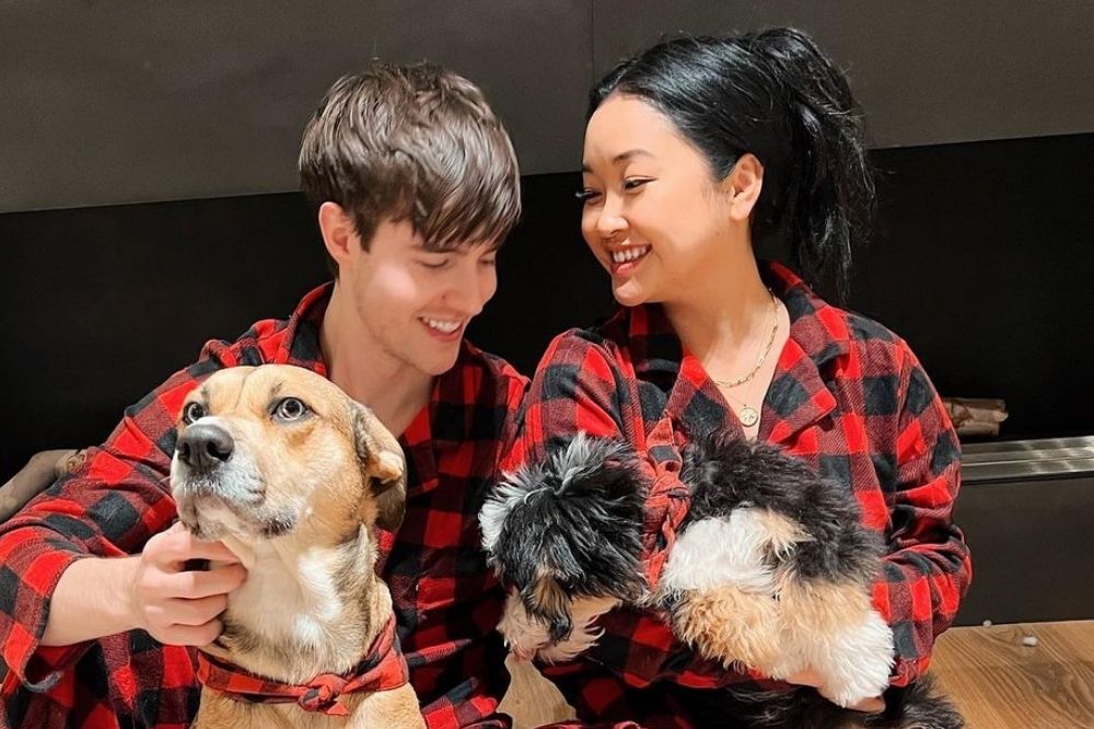 Lana Condor e Anthony De La Torre com roupas xadrez em vermelho e preto segurando seus cachorrinhos e sorrindo