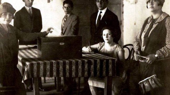 Curiosidades sobre a conquista do direito ao voto feminino no Brasil Foto em preto e branco de Celina Guimarães se alistando para ter o direito de votar. Ela está sentada a uma mesa, escrevendo em um pedaço de papel