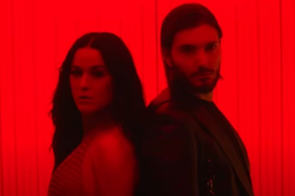 Katy Perry e Alesso em clipe de When I'm Gone; eles estão com expressões sérias de costas um para o outro olhando para frente com luzes vermelhas iluminando o ambiente e os artistas