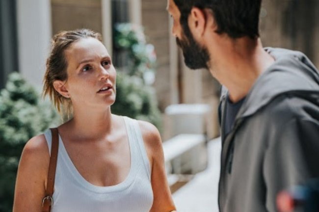 Uma mulher de regata branca e bolsa conversando com um homem de costas.