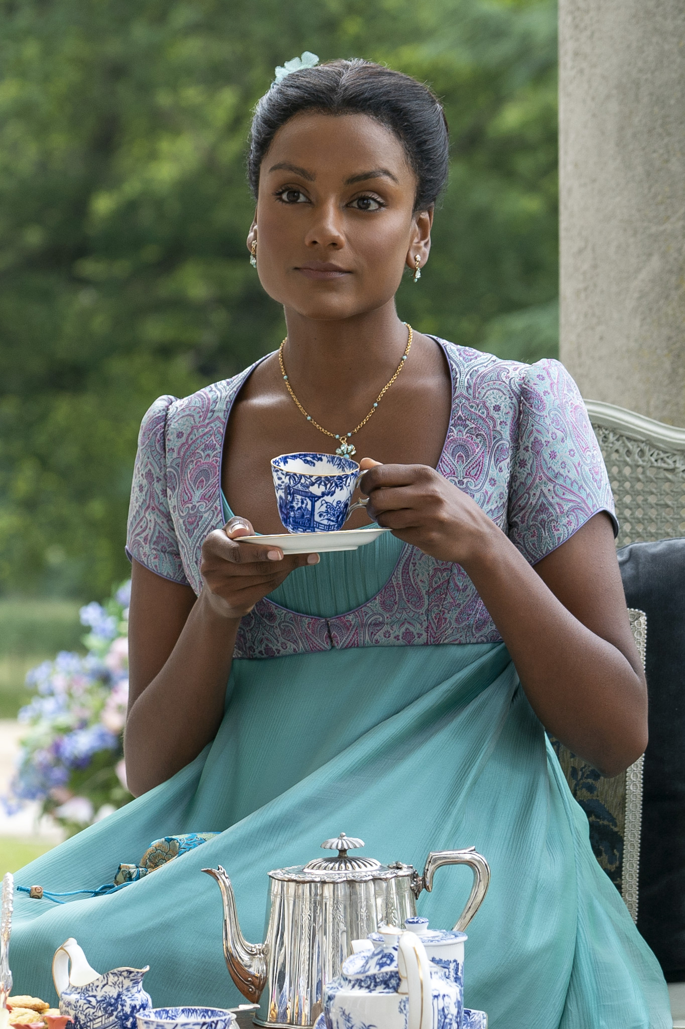 BRIDGERTON_203_Unit_04675RC Imagem mostra Simone Ashley caracterizada como Kate Sharma com vestido azul que segue a paleta de cores em tons de joias, enquanto toma chá em cena do 3º episódio da segunda temporada de Bridgerton.