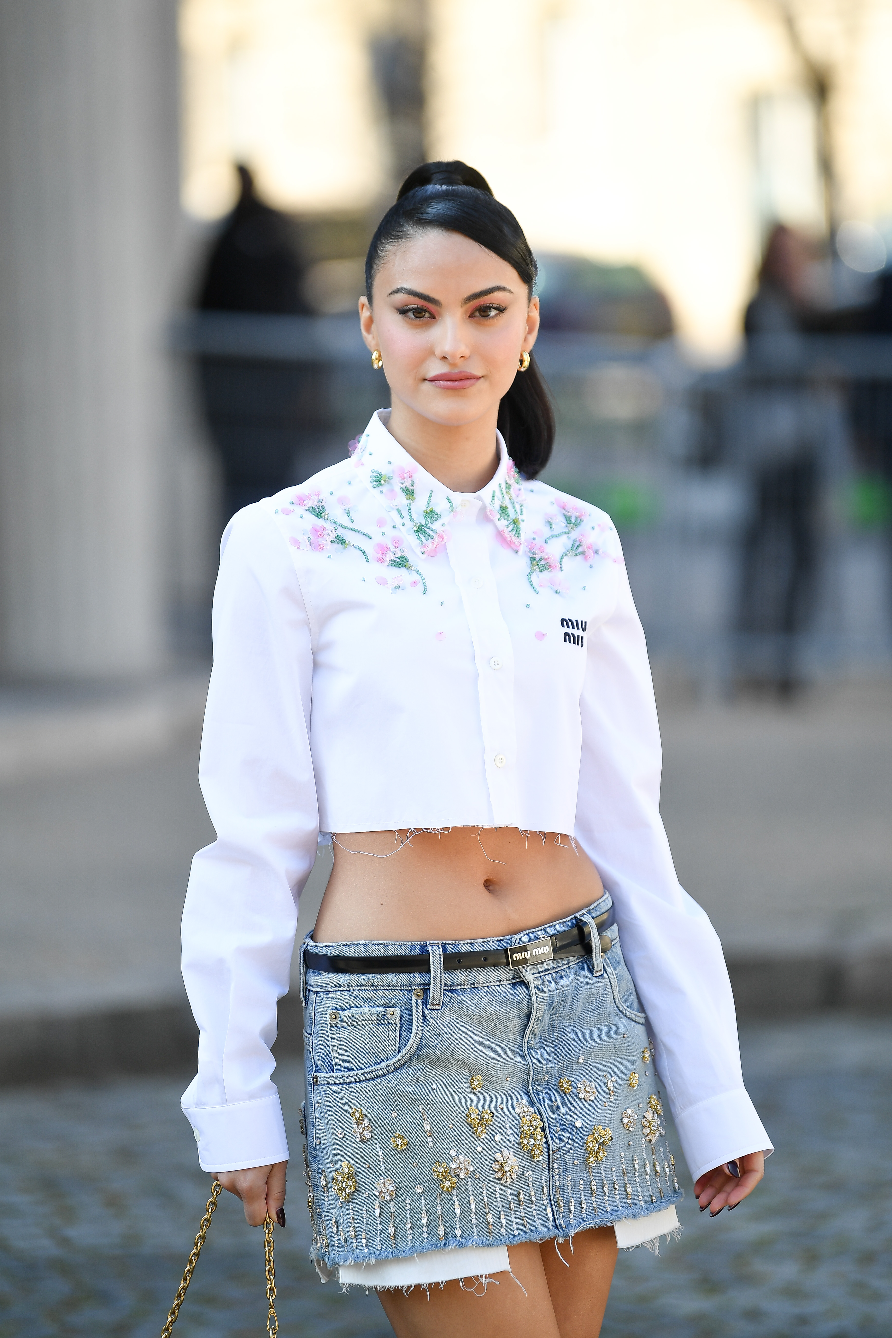 Miu Miu : Outside Arrivals – Paris Fashion Week – Womenswear F/W 2022-2023 Camila Mendes usando camisa branca cropped, minissaia jeans e cabelo preso em rabo de cavalo alto