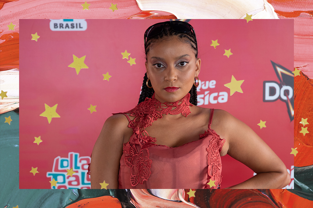 MC Tha no Lollapalooza BR 2022; ela está posando no backdrop do Lounge Doritos com uma roupa vermelha, uma das mãos na cintura e expressão séria; a moldura é uma textura de tintas nos tons de vermelho, verde, rosa, branco e laranja com estrelas amarelas como decoração