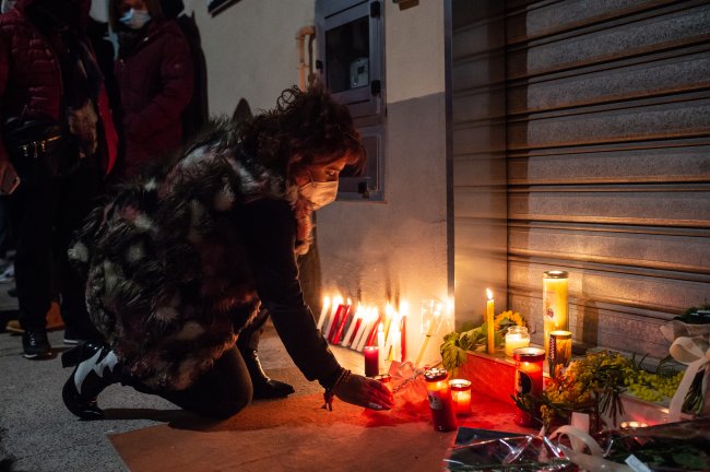 A cada 8h uma mulher foi vítima de feminicídio no Brasil em 2021 Foto de uma mulher ajoelhada acendendo uma vela em um memorial feito para uma mulher vítima de feminicídio. Está de noite.