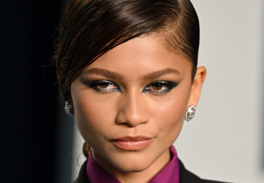 Foto da Zendaya na Vanity Fair de 2022 com um look com blazer e gravata e maquiagem com esfumado preto nos olhos. Ela olha para o lado e não sorri.