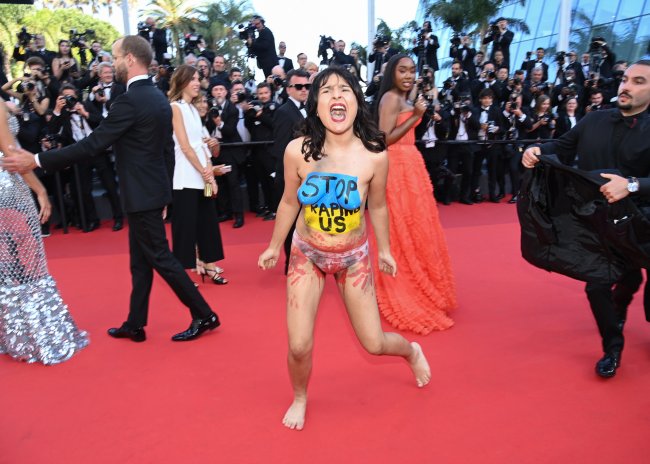 Foto de uma mulher seminua, apenas de calcinha, protestando no tapete vermelho do Festival de Cannes. Ela está com a bandeira da Ucrânia pintada no peito, sob os dizeres 