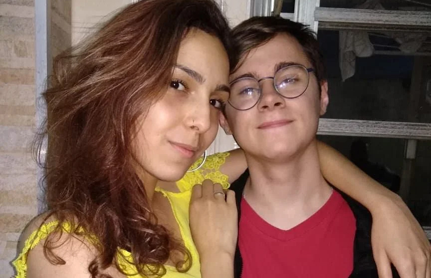 Foto de Isabela abraçada a Rafael Miguel. Ela tem cabelo castanho e usa uma blusa amarela. Ele usa óculos e uma camiseta vermelha.