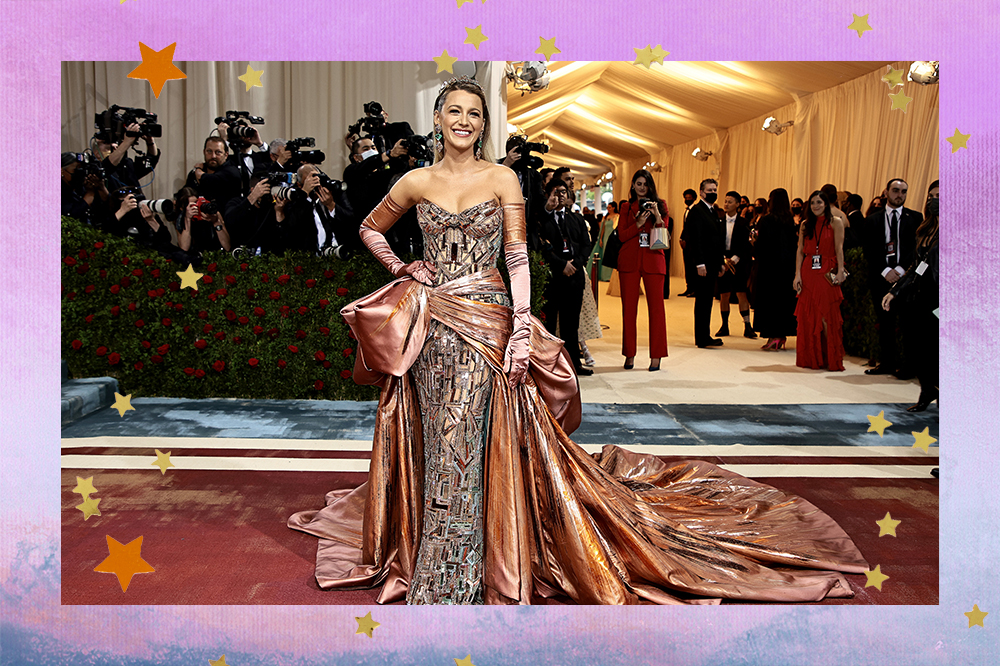 Imagem mostra Blake Lively usando vestido cobreado no tapete vermelho do MET Gala 2022, no Metropolitan Museum of Art em 02 de maio de 2022 na cidade de Nova York. A montagem segue acompanhada de uma borda lilás e estrelinhas douradas espalhadas.