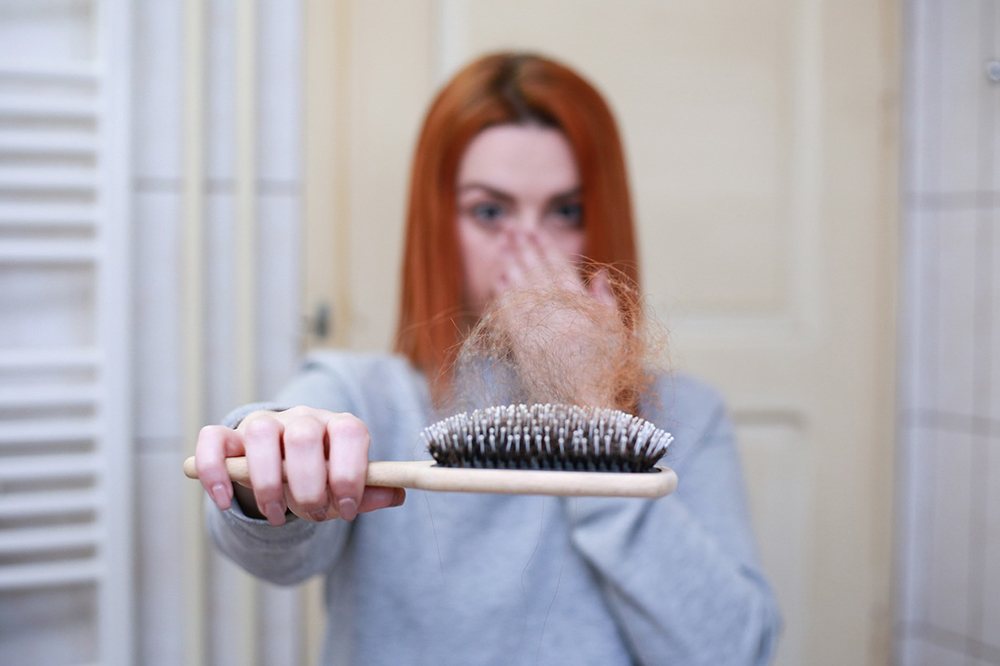 Garota mostrando escova com cabelo que caiu e com mão na boca fazendo expressão de surpresa