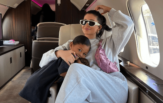 Kylie Jenner e Stormi Webster abraçadas em jatinho. Kylie está usando conjuntinho de moletom cinza e bolsa Le Cagole rosa, da Balenciaga