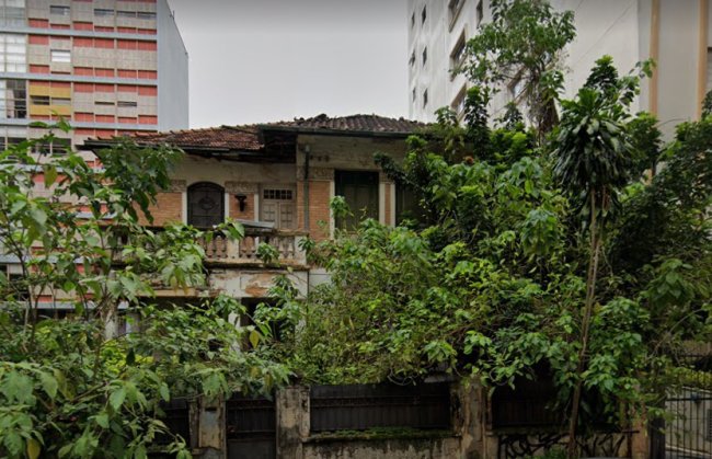 Foto de um casarão abandonado, de tijolos e cheio de árvores no quintal