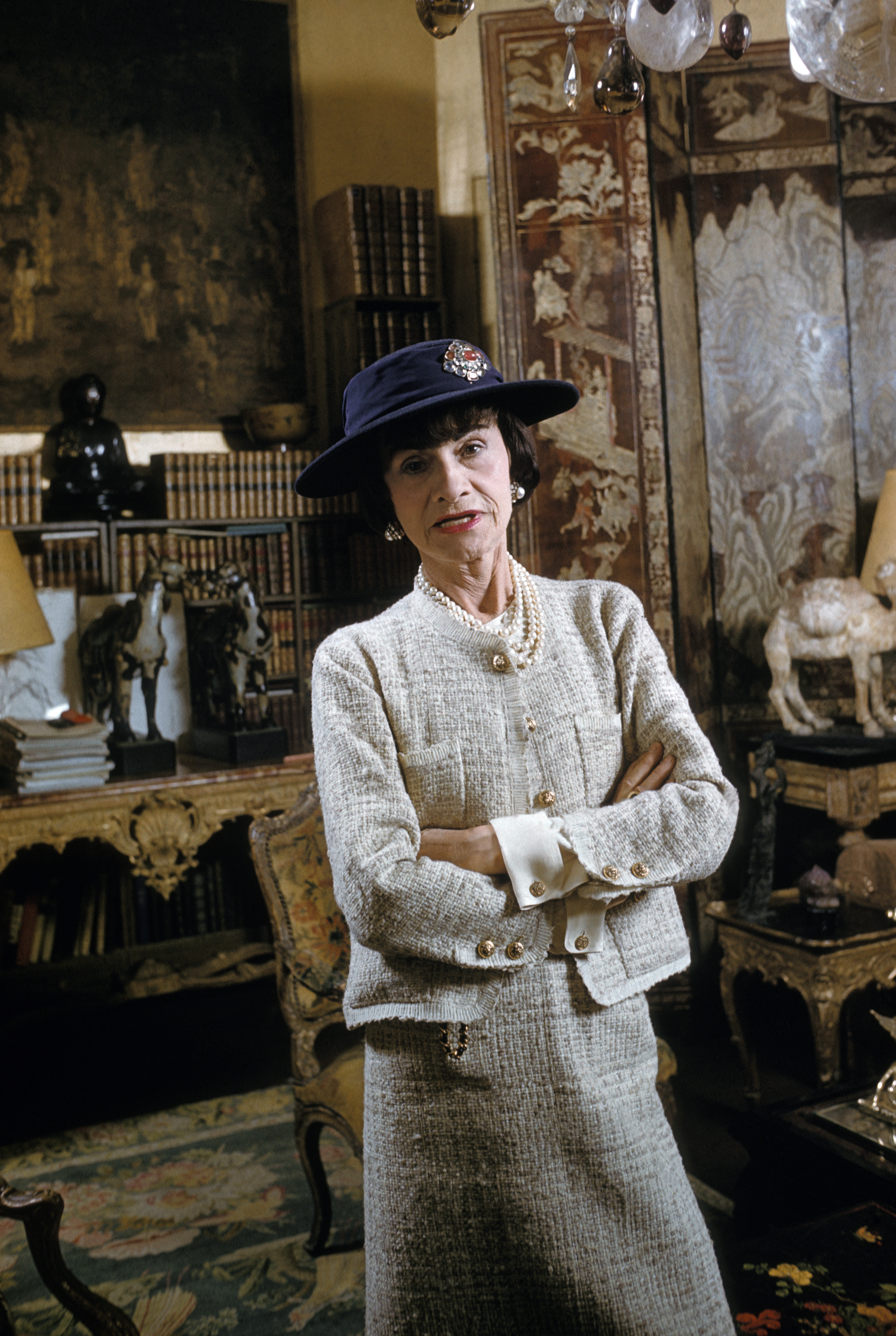 Coco Chanel Coco Chanel em seu apartamento na rue Cambon, em Paris, em 1954, usando chapéu e tailleur de tweed com botões dourados