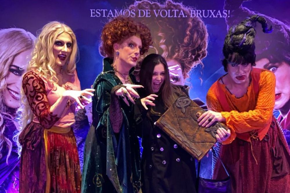 Menina posando para foto com drag queens vestidas de bruxas