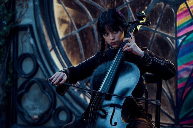 WEDNESDAY_105_Unit_05238RC2 Jenna Ortega como Wandinha Addams em série da Netflix; ela está tocando um violoncelo com uma expressão séria e vestindo roupas pretas