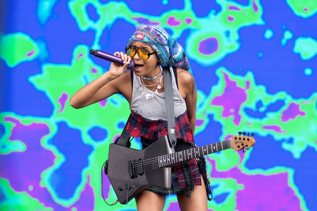 Willow Smith no Reading Festival em agosto de 2022 cantando e tocando guitarra com regata branca e minissaia com estampa xadrez