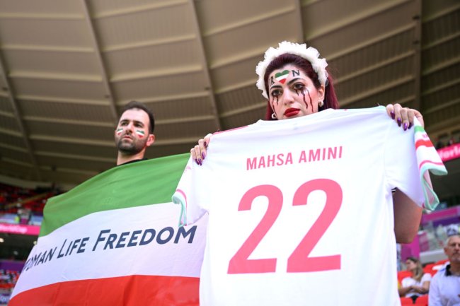 DOHA, QATAR - NOVEMBER 25: Fans hold up a shirt with the name of Mahsa Amini and a flag advocating for women's rights prior to the FIFA World Cup Qatar 2022 Group B match between Wales and IR Iran at Ahmad Bin Ali Stadium on November 25, 2022 in Doha, Qatar. People have continued demonstrating in Iran over the death of Mahsa Amini in September. Mahsa Amini fell into a coma and died after being arrested in Tehran by morality police, for allegedly violating the country's hijab rules. (Photo by Matthias Hangst/Getty Images)