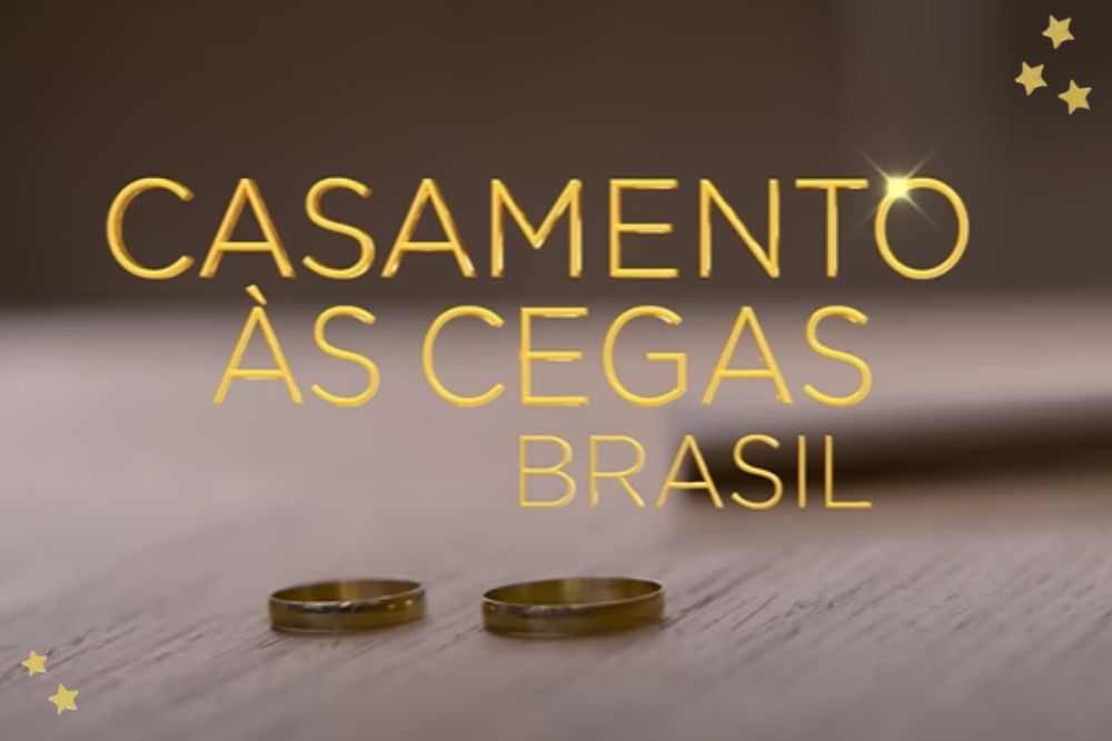 Duas alianças em uma mesa de madeira com o título "Casamento às cegas Brasil" em dourado no centro da foto; estrelas amarelas decoram a imagem