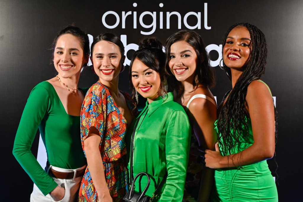 Elenco de As Five posando em frente backdrop com logo da série.