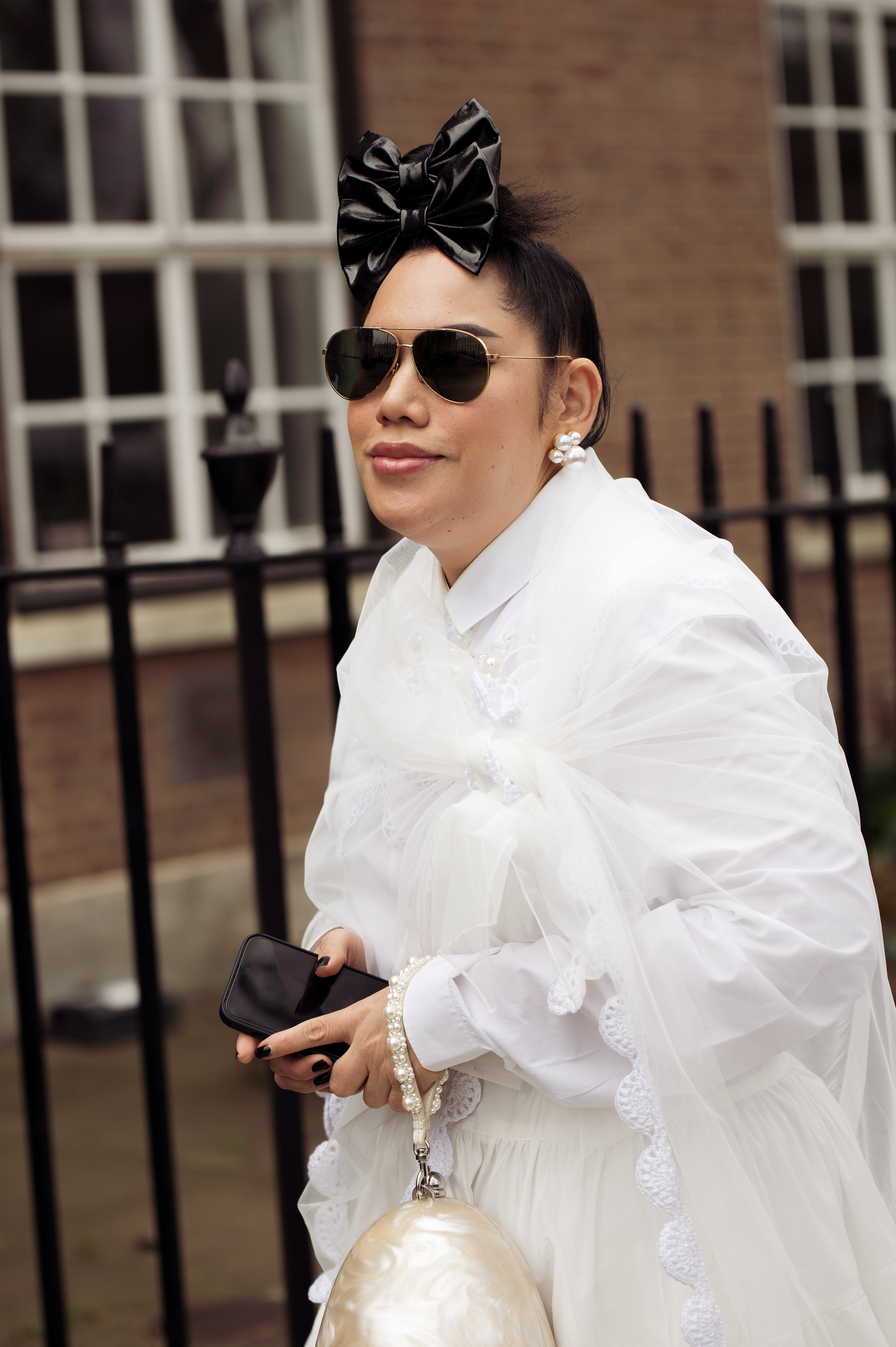 Mulher usando look branco, óculos de sol e laços pretos na frente do cabelo no street style da semana de moda de Londres