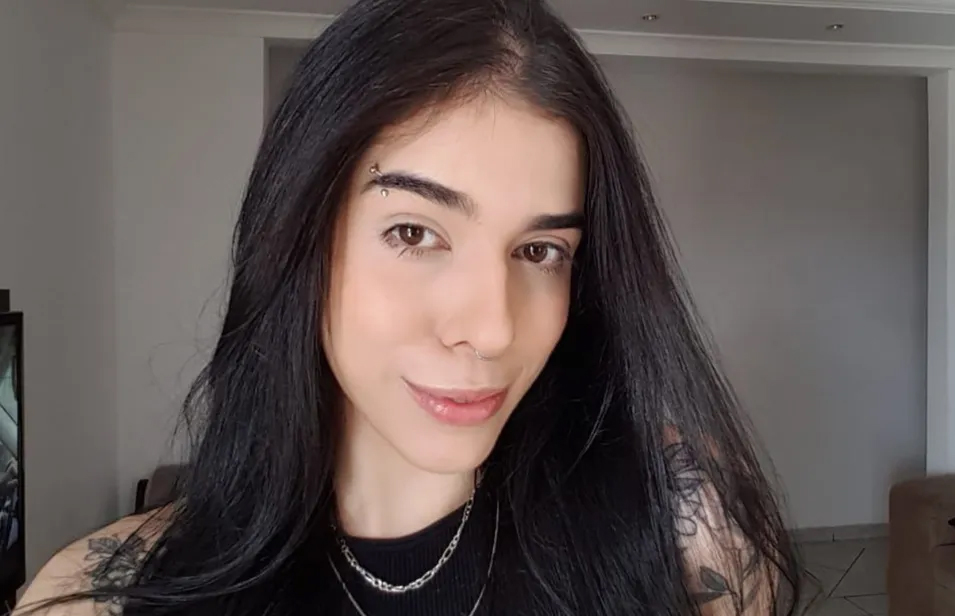 Thais Medeiros de Oliveira. Ela é uma mulher branca, com o cabelo preto, liso e comprido, e um piercing na sobrancelha