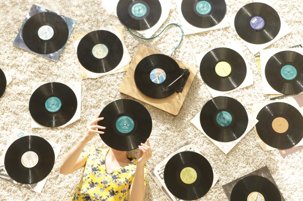 Mulher segurando um disco de vinil e deitada em volta de vários discos