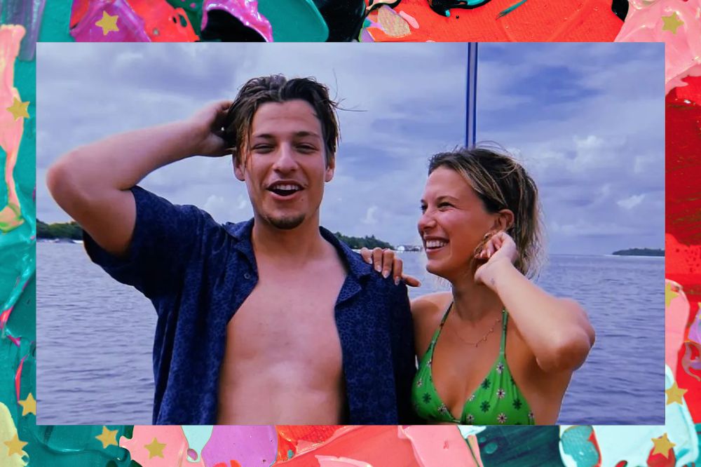 Jake Bongiovi e Millie Bobby Brown sorrindo em foto; ela está olhando para ele em um barco com o mar ao fundo enquanto ele diz algo; os dois passam a mão pelos cabelos e estão abraçados; a margem é uma textura nas cores rosa, lilás, verde, roxo, vermelho e azul com estrelas amarelas como decoração