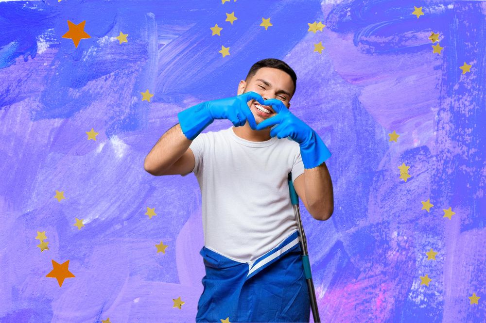 Um homem vestindo camiseta branca e calça azul. Faz um coração com as mãos que estão cobertas por luvas azuis