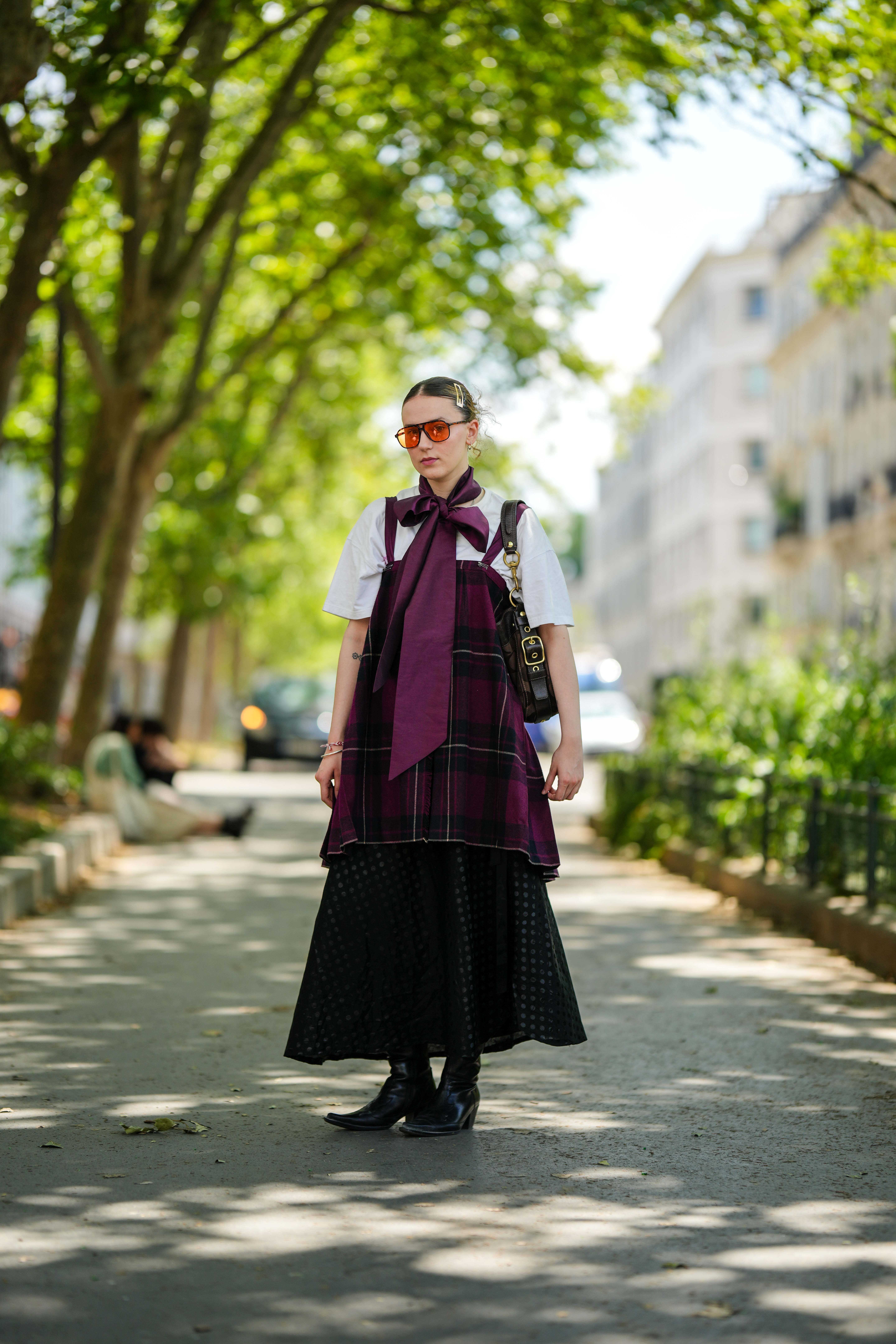 Street Style – Paris Fashion Week – Menswear Spring/Summer 2024 : Day Five Look no street style da semana de moda masculina de primavera-verão 2024 em Paris. Mulher usando camiseta branca sobreposta a peça xadrez e saia com bota western preta e óculos de lentes amareladas