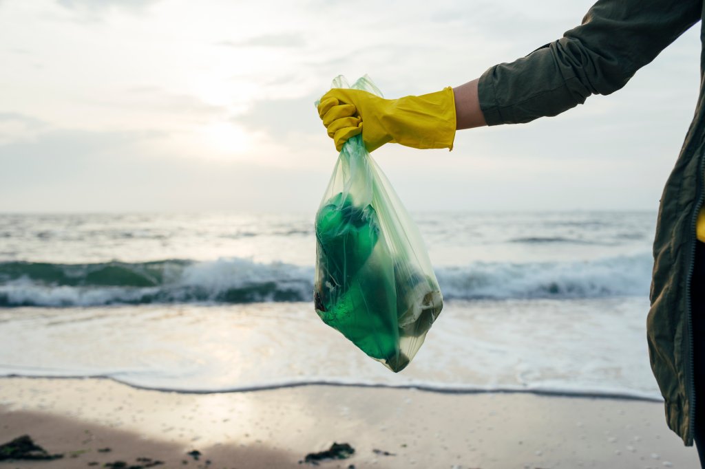 Mid adult woman holding garbage bag while standing at beach