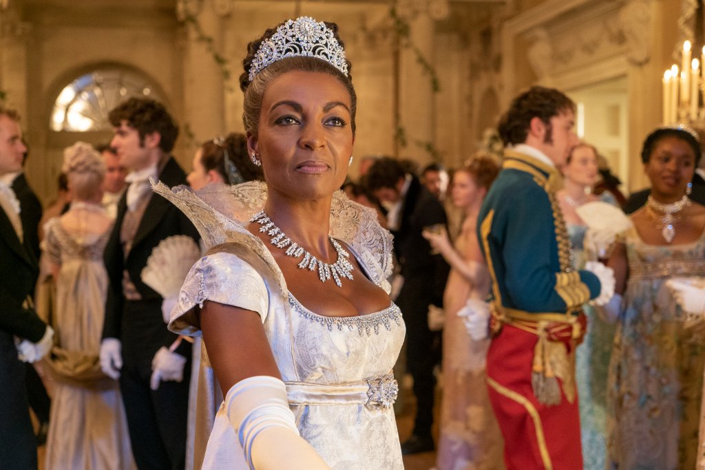 Adjoa Andoh como Lady Danbury em Bridgerton; ela está com vestido de festa no meio de um salão com pessoas ao redor; sua expressão é neutra