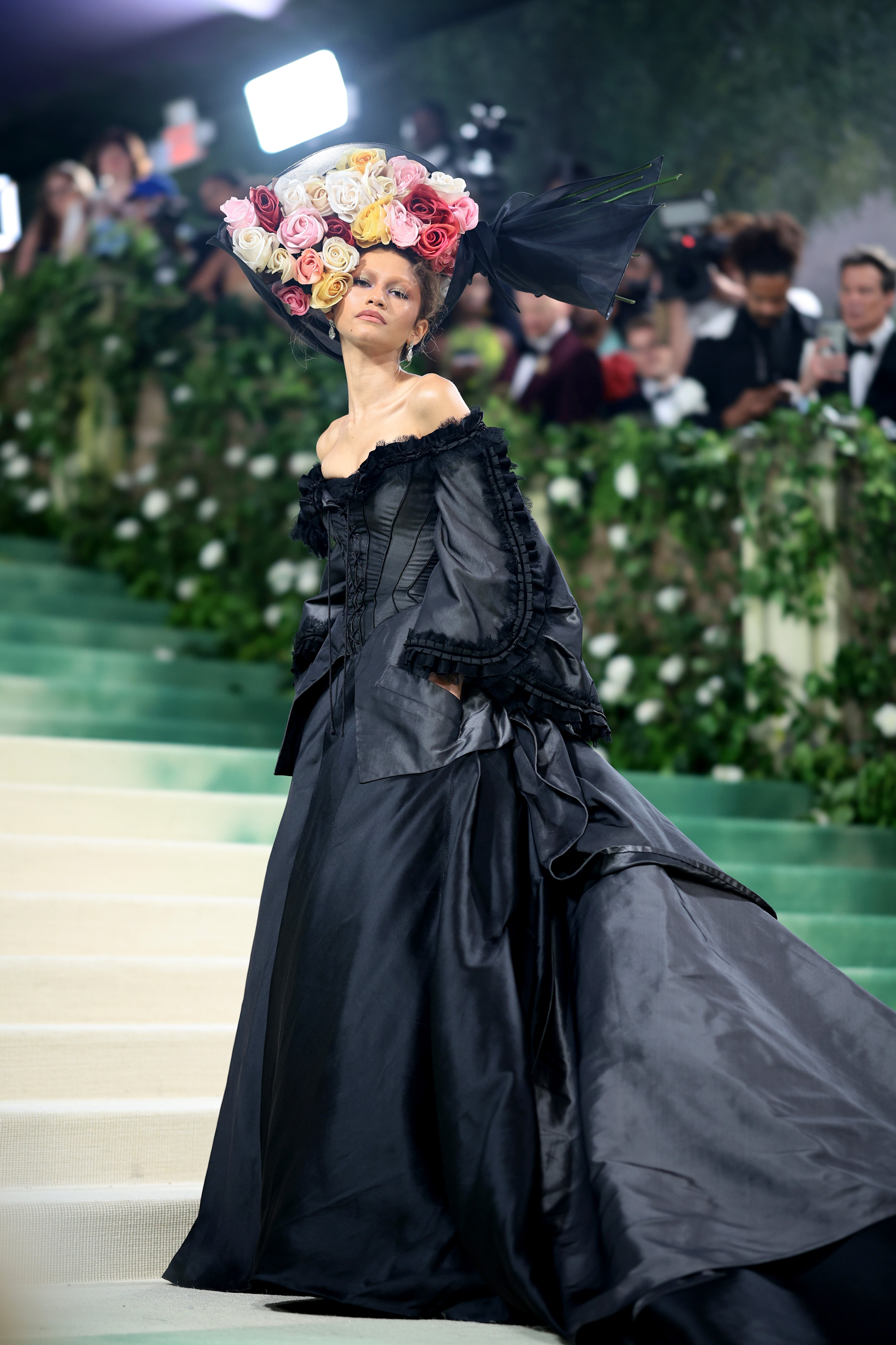 Zendaya posando para foto com vestido vintage preto e acessório para cabeça com aplicação de flores