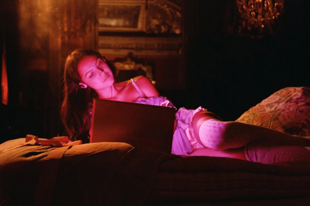 Mulher deitada na cama usando notebook, com iluminação quente e clima íntimo.